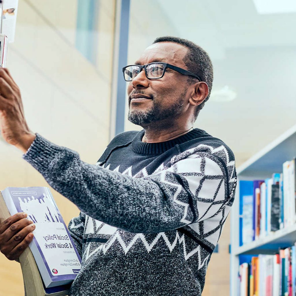 An older mature male student picking out books in the libary