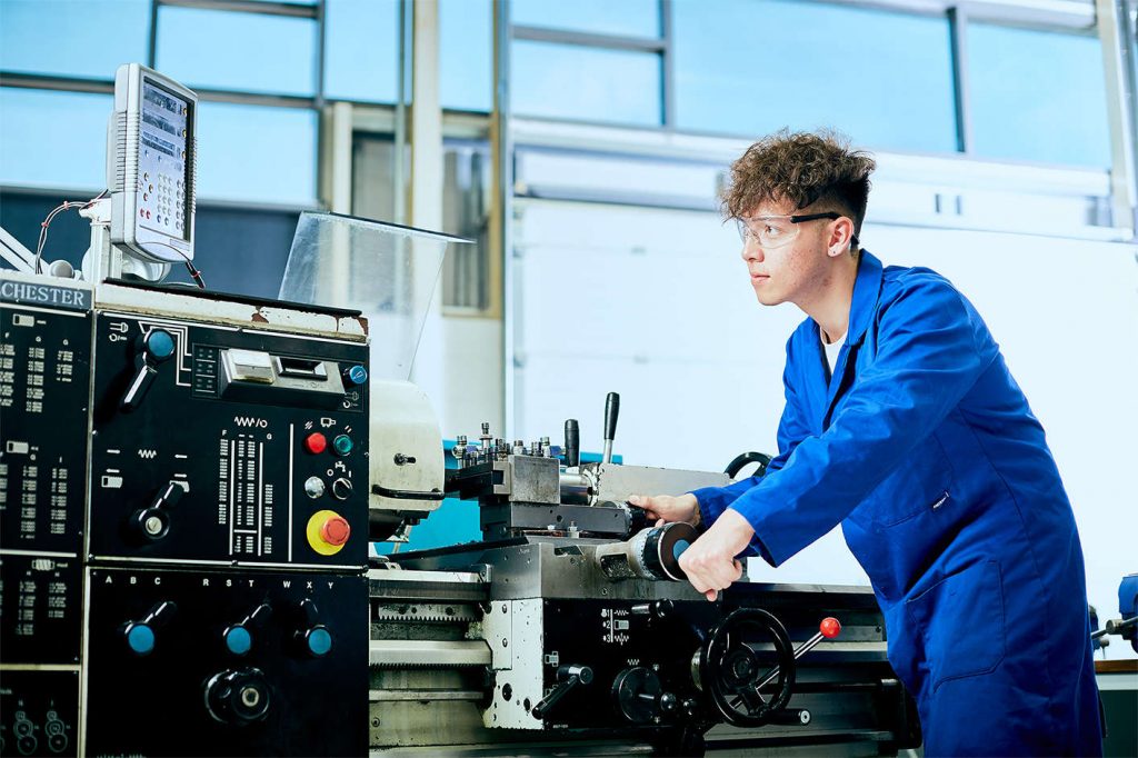 A young male kirklees student wearing blue overalls using a large metal machine