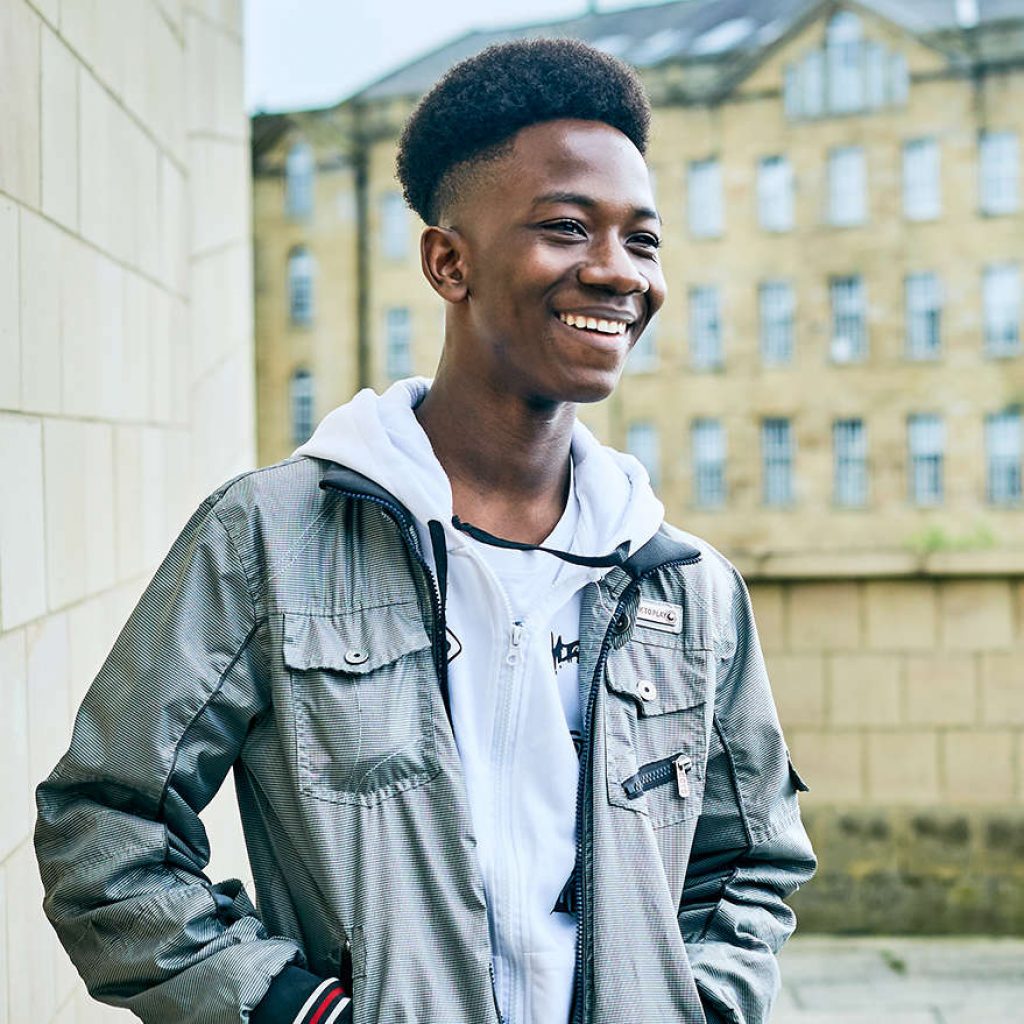 a young black male stood outside in front of a building smiling