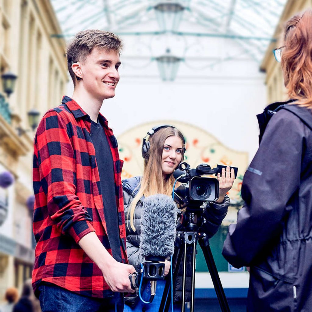 A film crew and interviewer speaking to a woman inside an old traditional victorian building