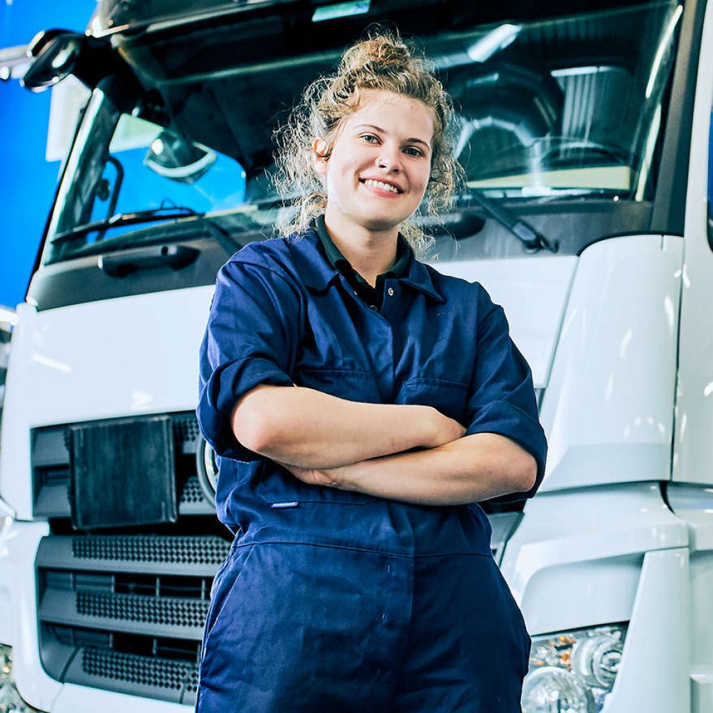 a female kirklees student wearing blue overalls stood in front of a truck
