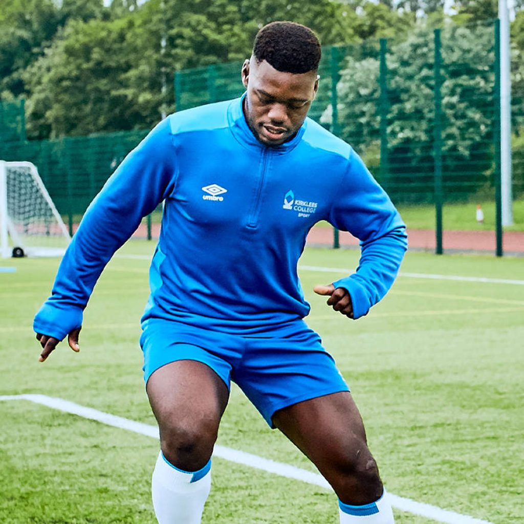 A young black student practising his football skills dribbling around cones on a 3G astroturf pitch