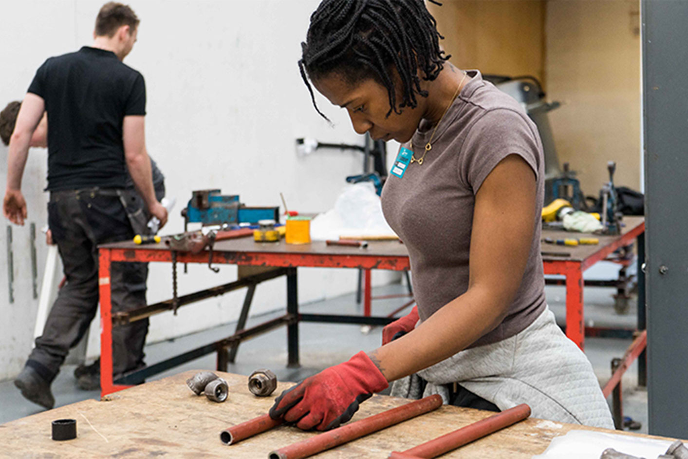 A young black female construction student cutting and measuring some pipe work