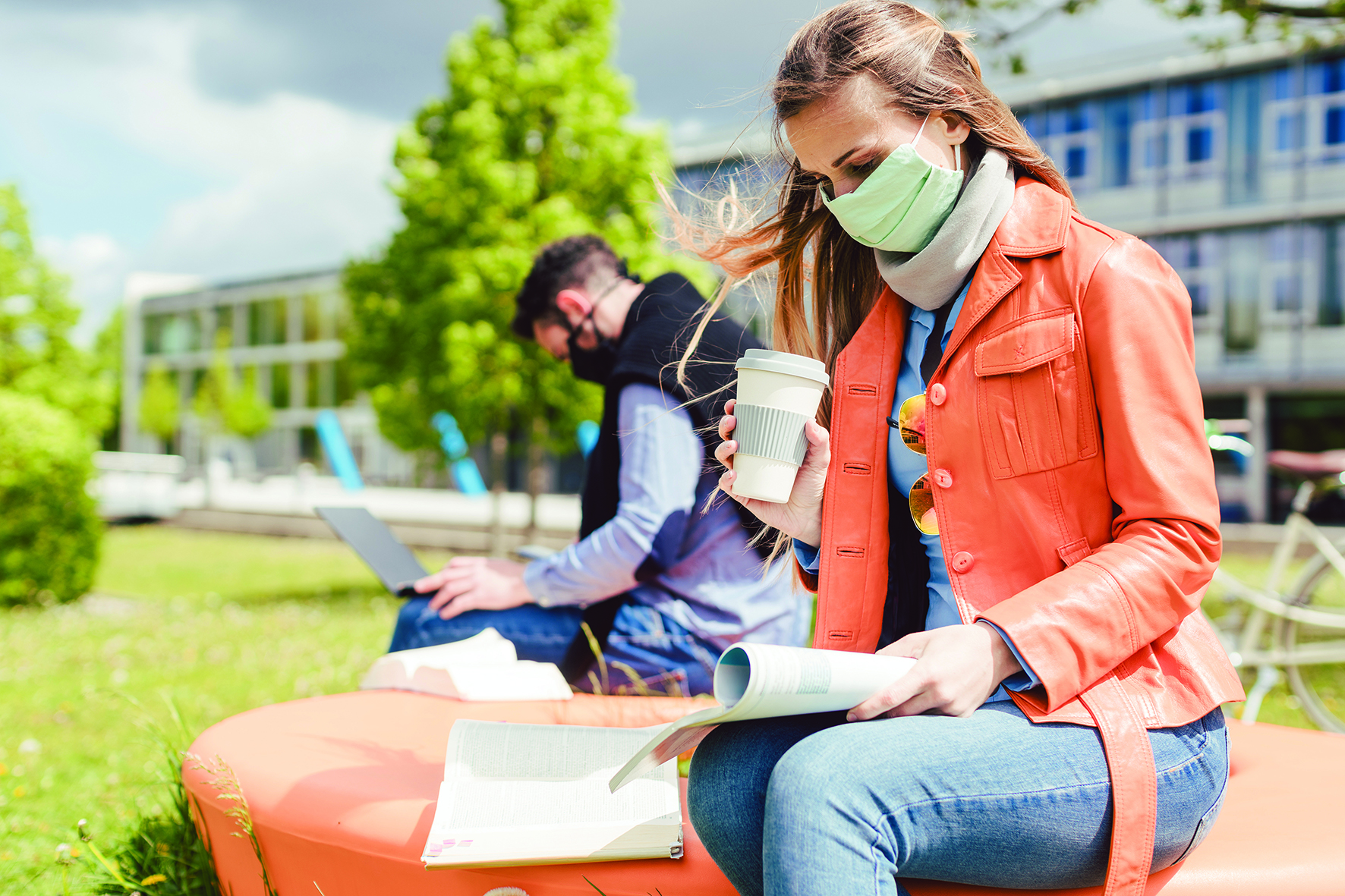 Woman sat with coffee cup on a bench with a mask on