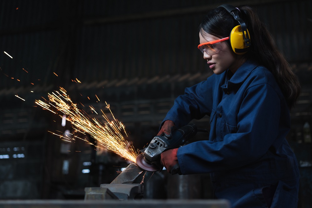 Diverse female immigrant metal worker using industrial machinery in manufacturing factory with sparks