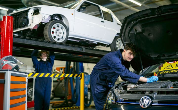 Two male students working on cars in the mechanics bay of the college