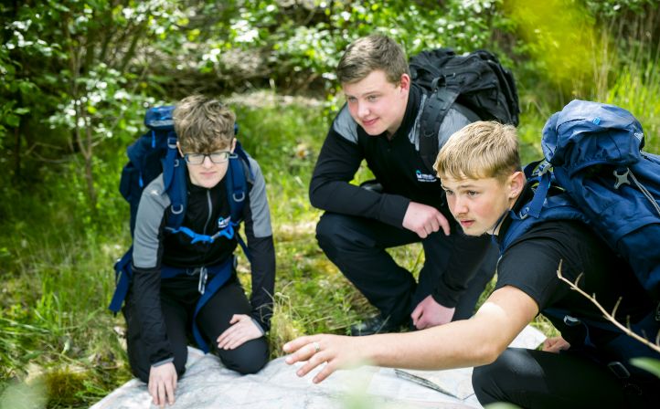 Three male students studying a map outdoors during an team building exercise