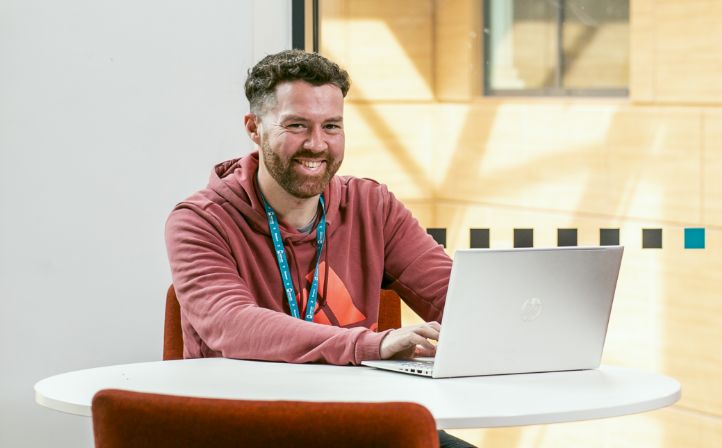 Mature student smiling at the camera and working on his laptop