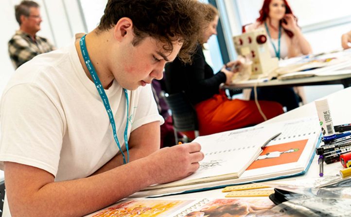 Male student sat sketching in a textiles classroom