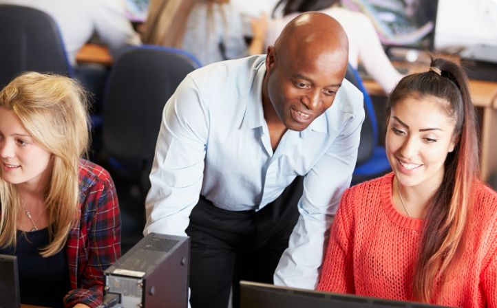 Two girls sat at their computers during an IT class with their tutor helping