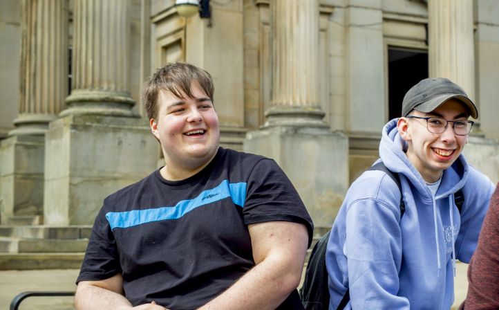 Two male student sat on stone steps in Huddersfield