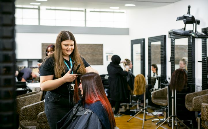 Female student straightening a ladies hair in the college salon