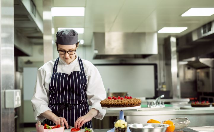 Female student chopping up fruit to put on top on a cake in the college kitchens