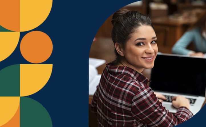 A young asian student looking at the camera and smiling whilst she works on her Laptop