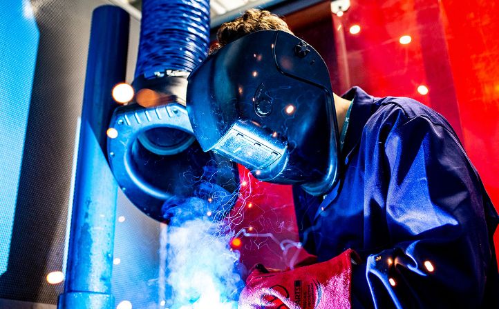 A welder in a mask with sparks flying and smoke appearing