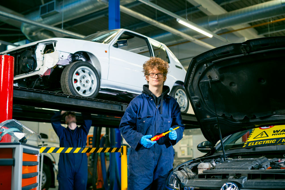Male Motor Vehicle Student Standing Beside Vehicle Bonnet While Holding Screwdriver and Smiling at the Camera