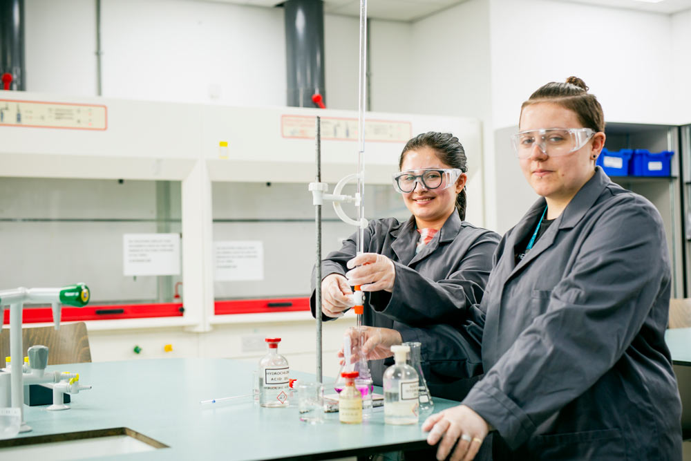 Two Science Students Performing Experiment in Science Laboratories and Smiling at the Camera