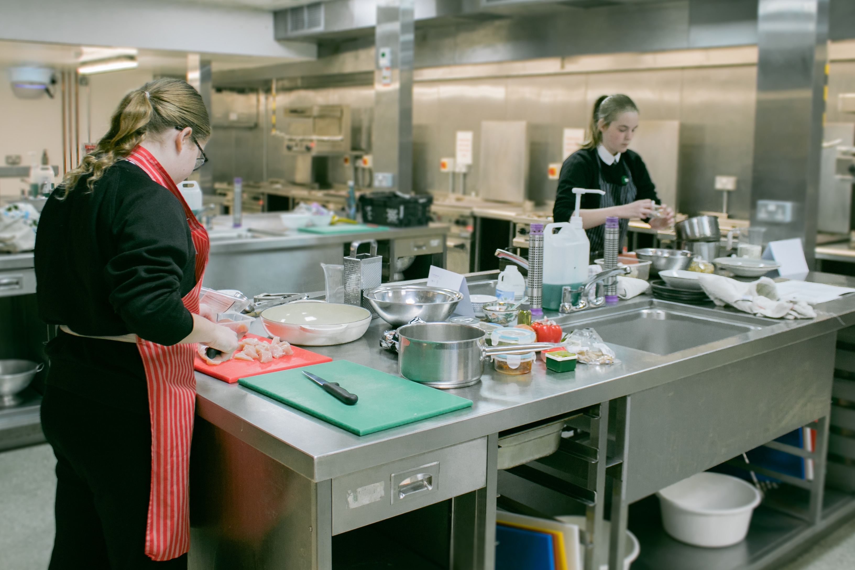 Two female students chopping and preparing food in stainless steel kitchen