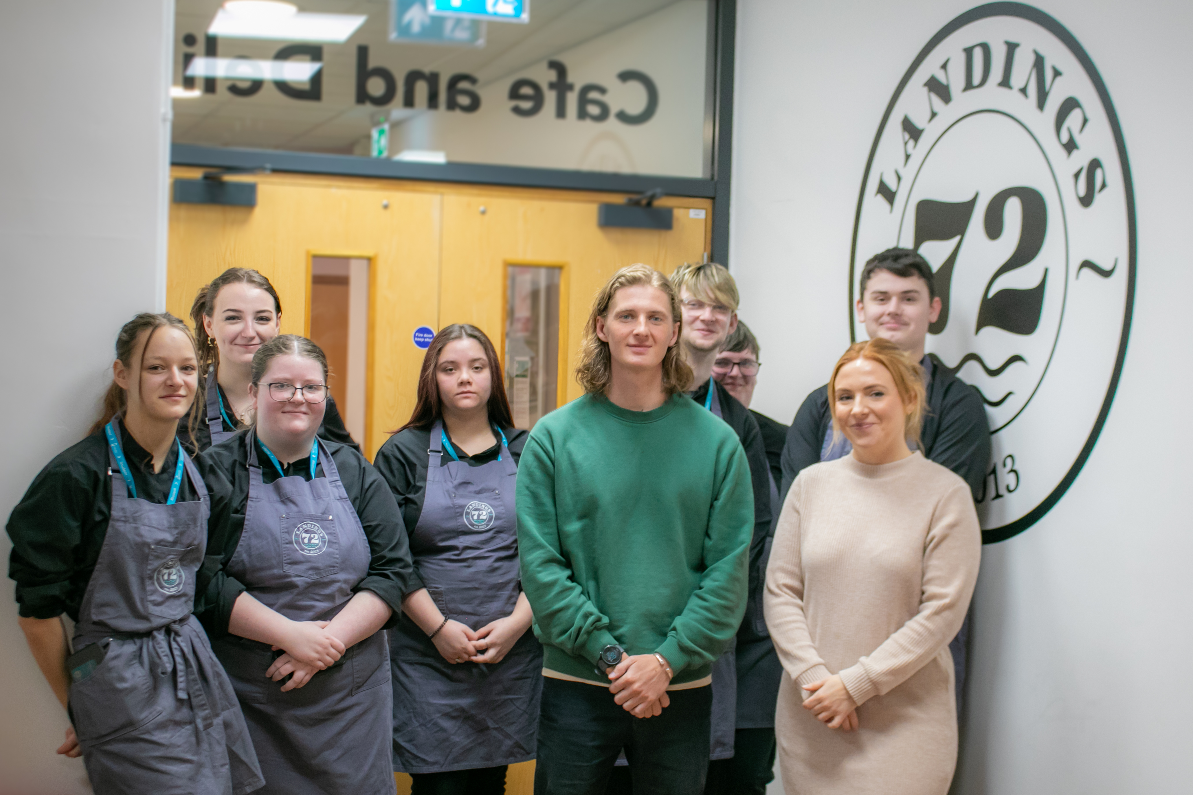 Cafe Culture students and representatives from Coffee Brothers pose for a photo in front of double doors and wall that says Landings 72