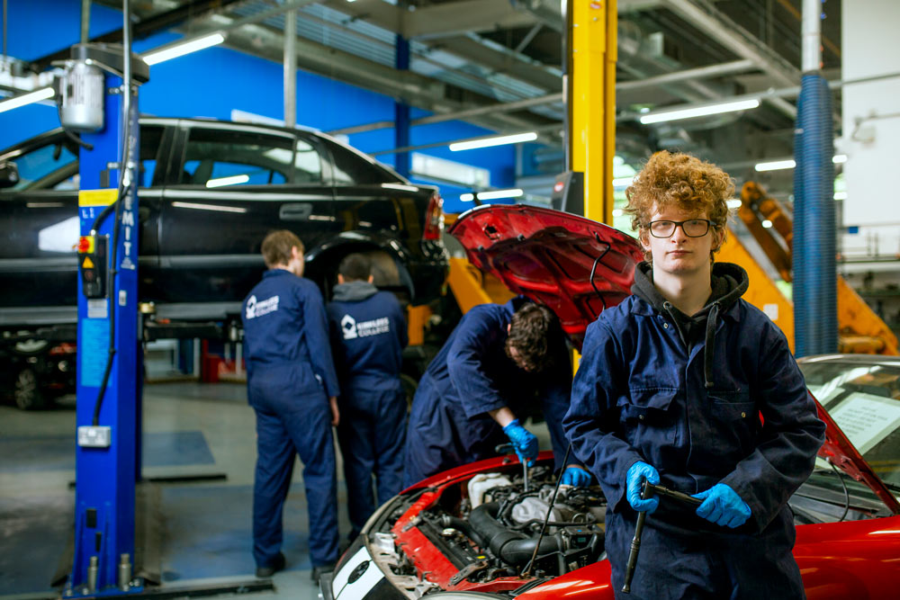 Two kirklees college students wearing work wear work on a car