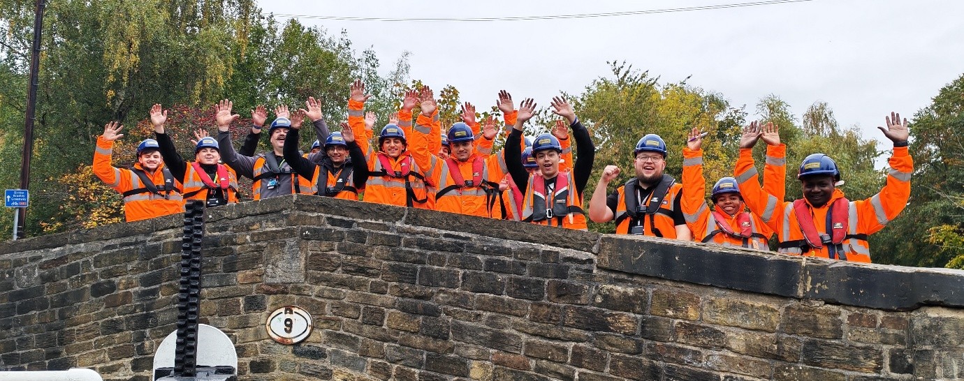Kirklees College students stand in high vis jackets on top of footbridge at Huddersfield Canal