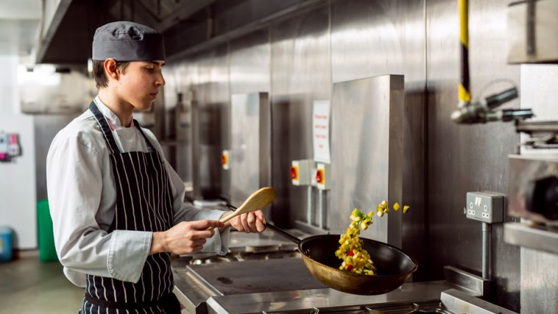 Action Shot of Male Hospitality and Catering Student Flipping Vegetables in Frying Pan