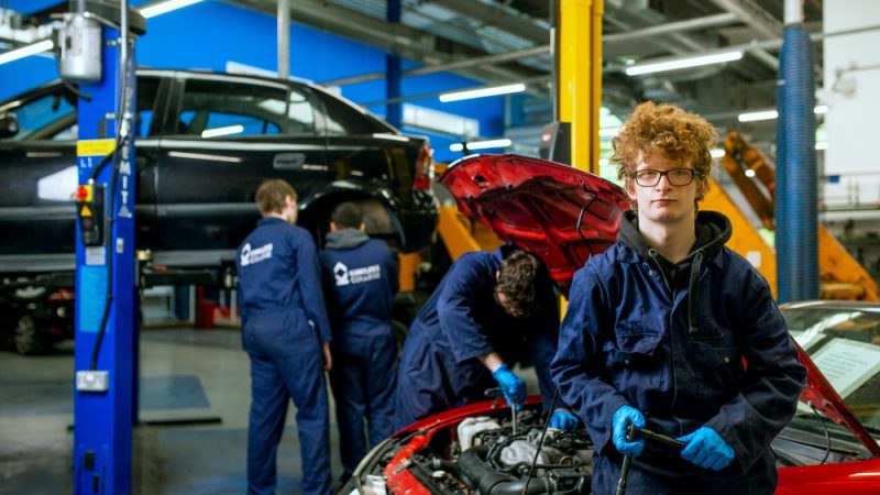 Male Motor Vehicle Student Smiling at Camera with Other Motor Vehicle Students Working in the Background