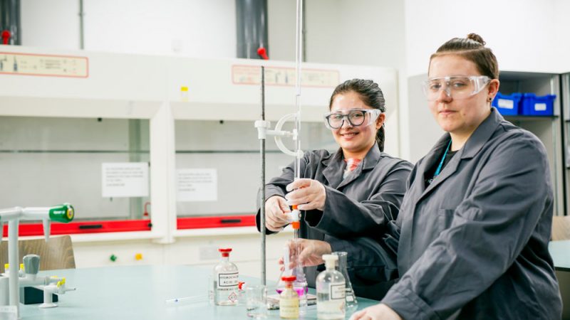 Two Science Students Performing Experiment in Science Laboratories and Smiling at the Camera