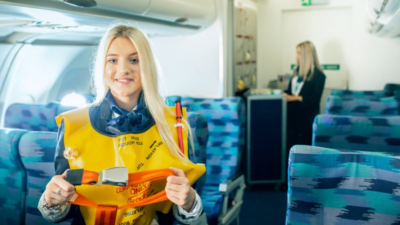 Female Travel and Tourism Air Cabin Crew Student Wearing Life Jacket in Mock Aircraft Cabin