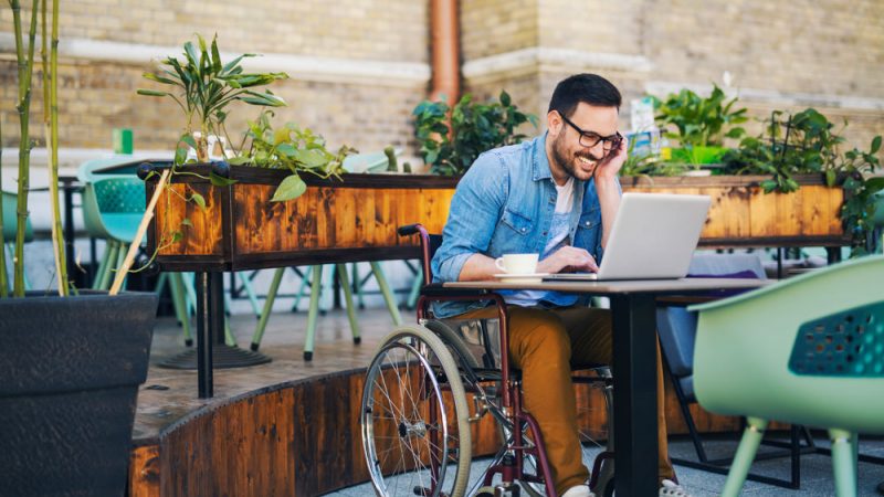 Smiling young handicapped man using laptop at cafe