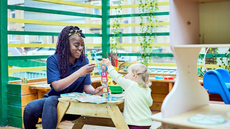 A young nursery teacher playing with a small toddler