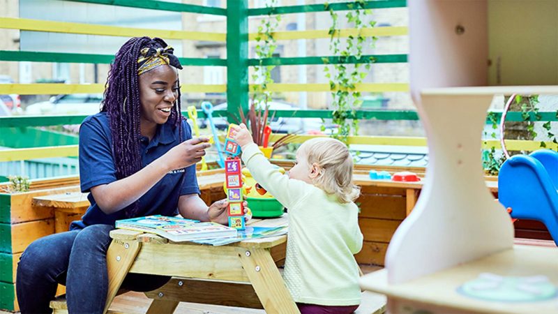 a young black nursery teacher playing with a small toddler