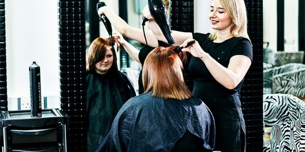 A young female hairdressing student giving a client a cut and blow