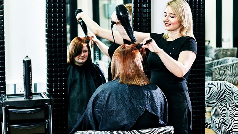 A young female hairdressing student giving a client a cut and blow