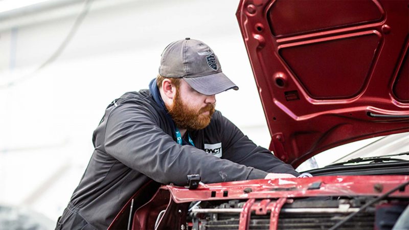 A young mechanic in Kirklees overalls wrking on a car