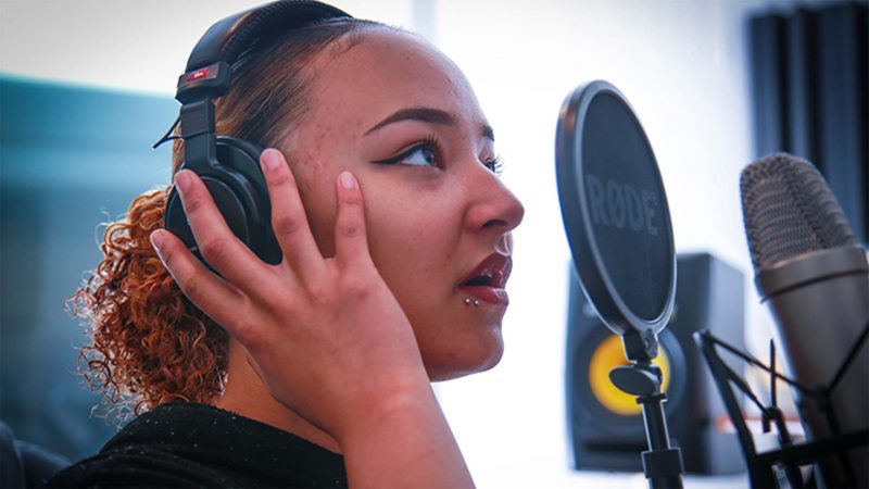 A young black female recording into a studio microphone