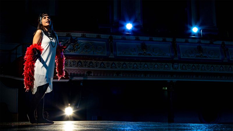 A young female performer stood on stage gazing off camera