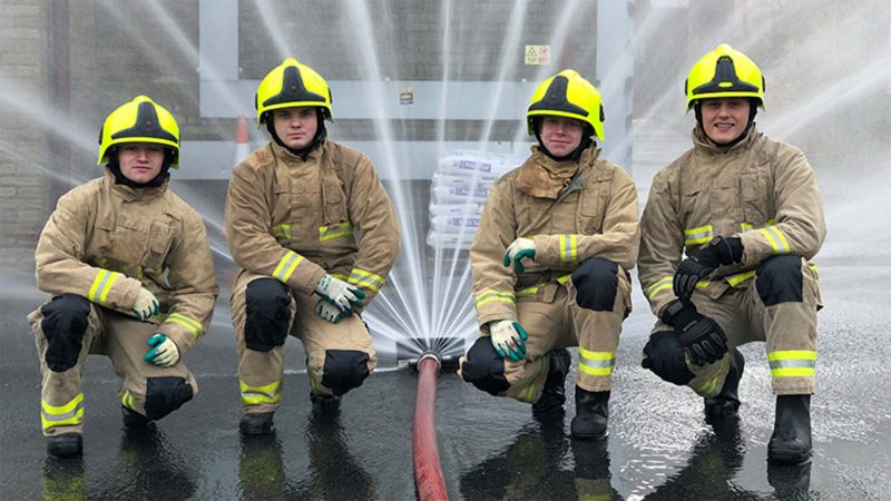 a group of firemen stood next to a hose
