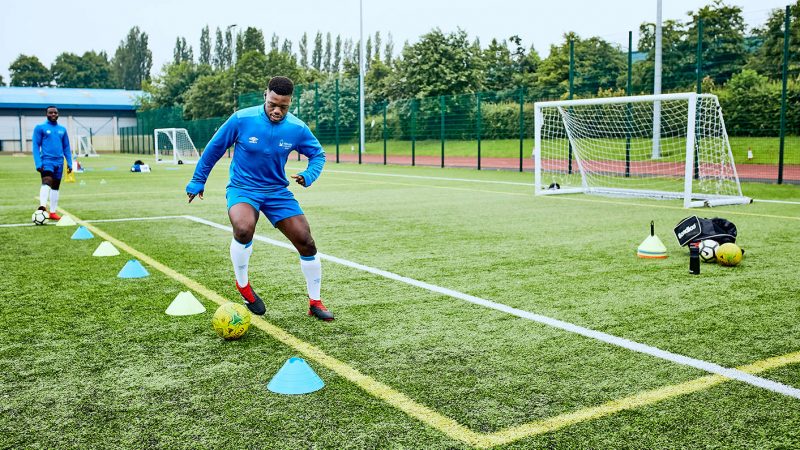 A young black student practising his football skills dribbling around cones on a 3G astroturf pitch